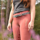 reitleggings mit handytasche und silikon vollbesatz im punkte design gürtelschlaufen glitzer strass gürtel mit gebissmotiv rothaarige frau mit grauen shirt glitzergürtel und reitleggings in der heide  